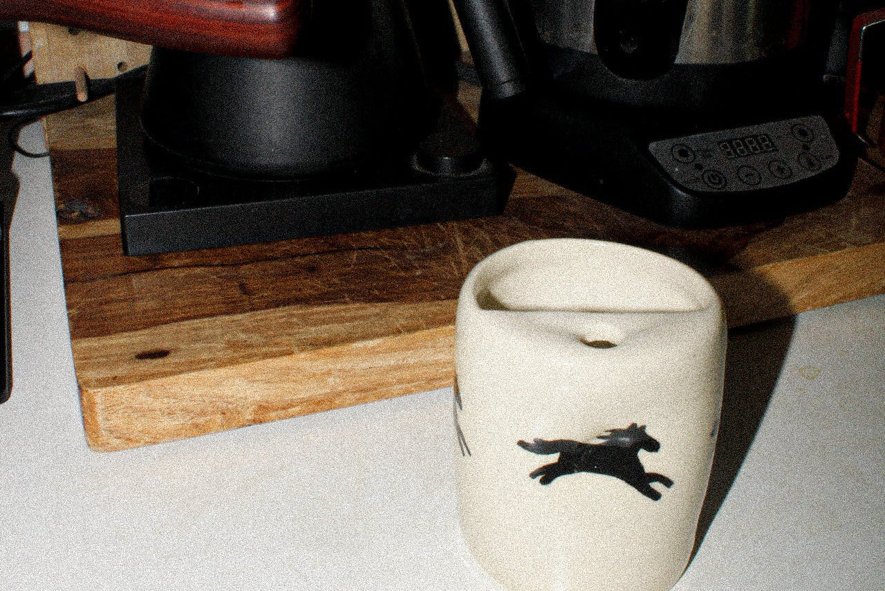 Ceramic mug with a black design on a kitchen counter with a kettle and other items.